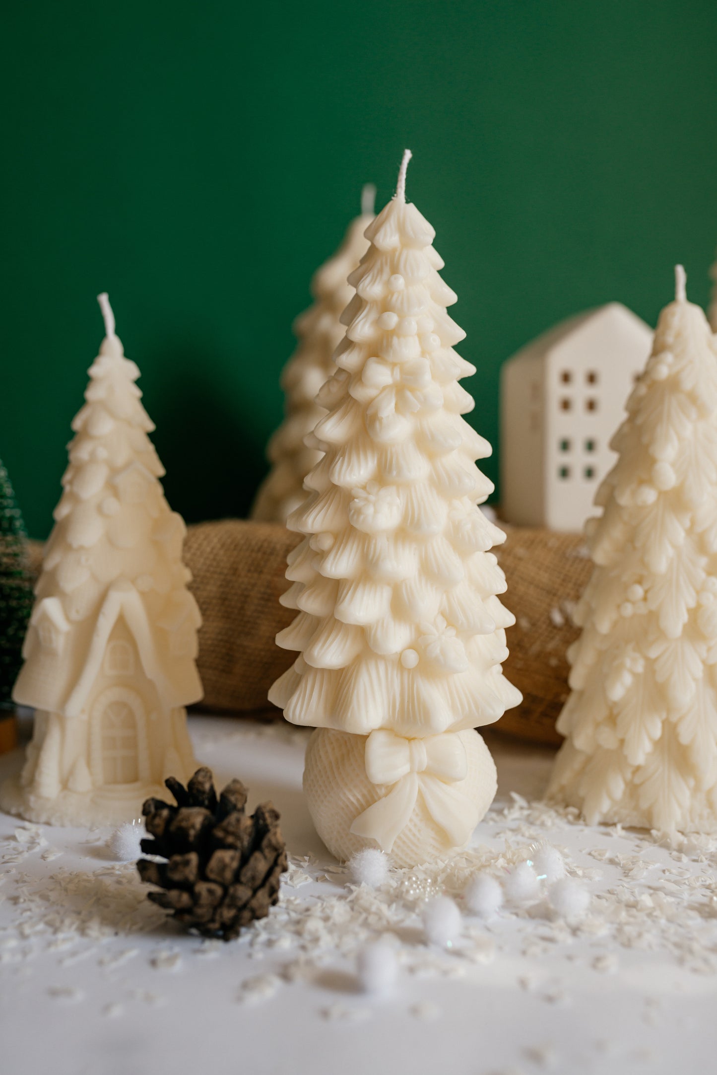 Creamy white soy wax candle shaped like a Christmas tree decorated with small bows and ribbons, standing on a round gift-sack base with a large bow.