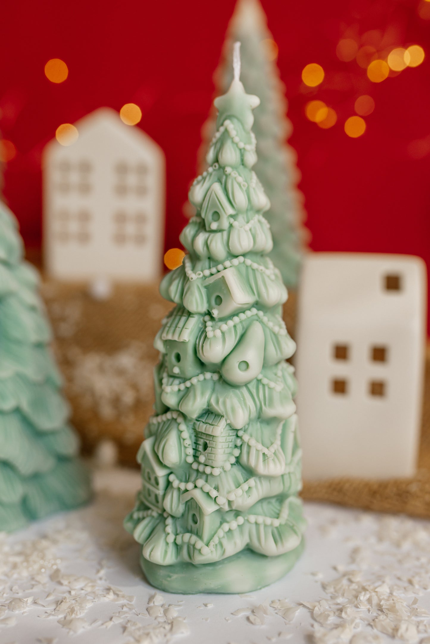 Close-up of a green soy wax candle shaped like a Christmas tree covered in many small, detailed houses and garlands.