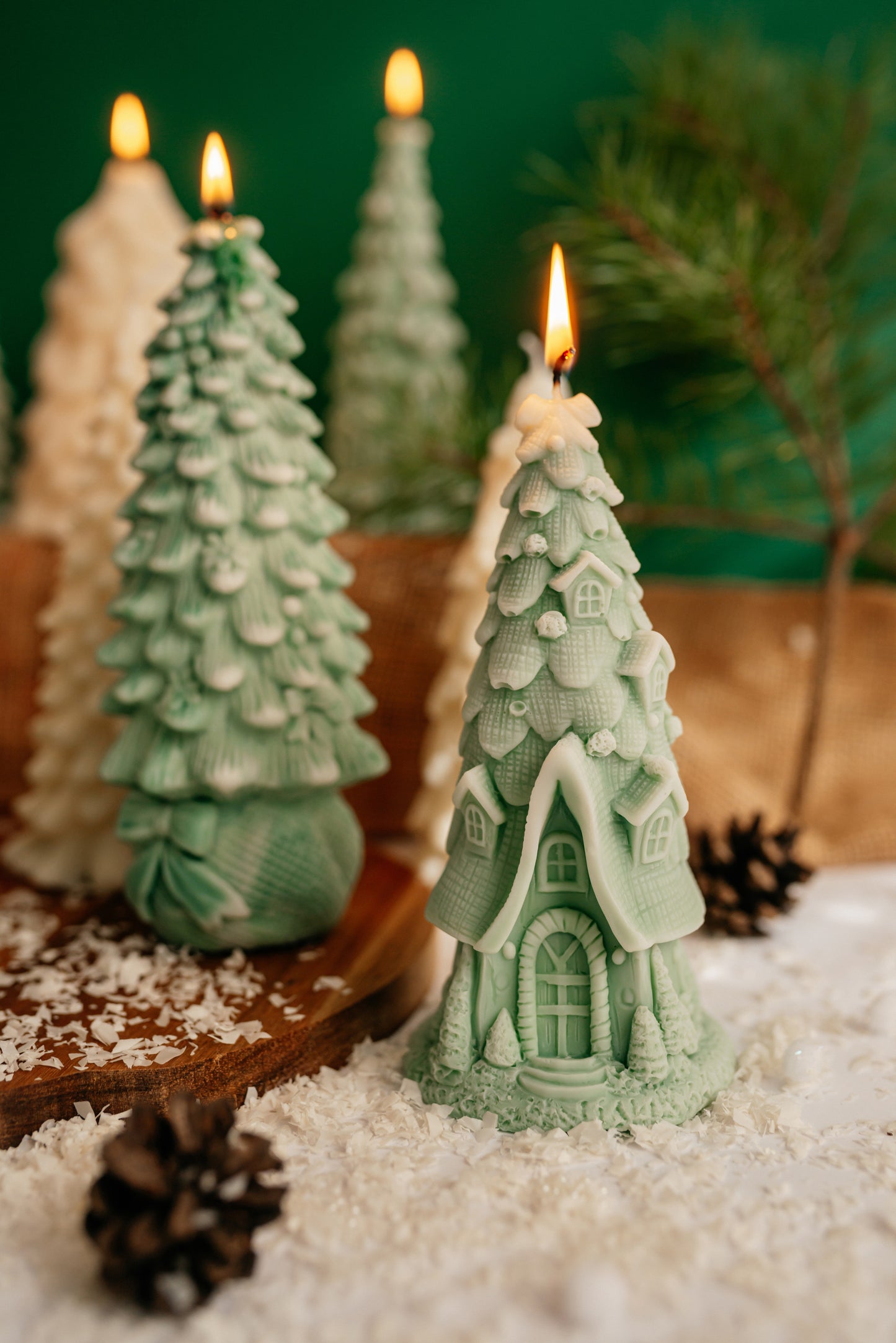 Green soy wax candle shaped like a fairy tale cottage with a steep tiled roof and arched door, standing next to a green Christmas tree candle.