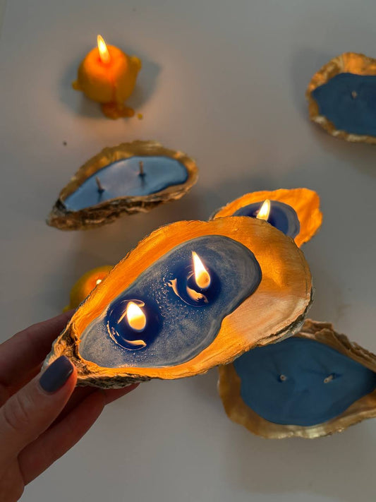 Hand holding a luxury gilded oyster shell candle with blue wax and two burning wicks