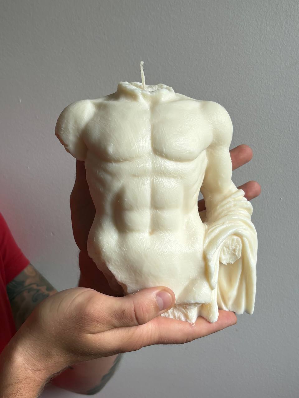 Front view of the large Greek statue male torso candle held by hand against a minimal background.