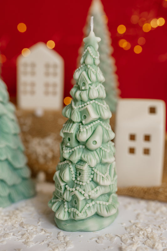 Close-up of a green soy wax candle shaped like a Christmas tree covered in many small, detailed houses and garlands.