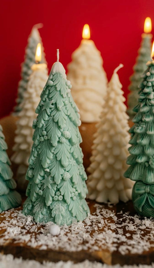 Close-up of a green soy wax candle shaped like a Christmas tree made of detailed leaves, decorated with berries and snowflakes.