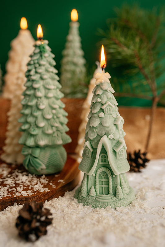 Green soy wax candle shaped like a fairy tale cottage with a steep tiled roof and arched door, standing next to a green Christmas tree candle.