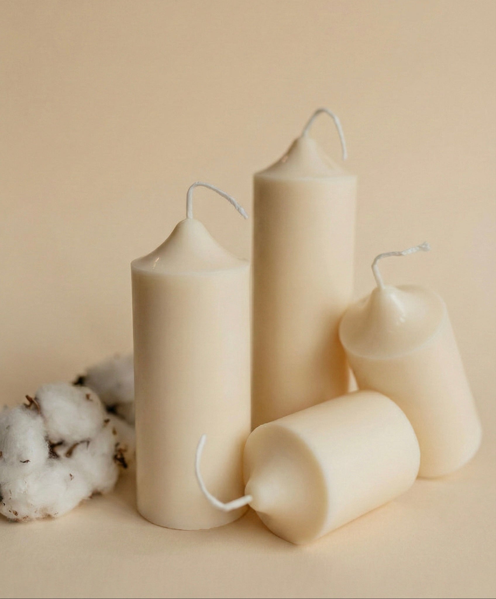 Set of beige candles on a beige background with cotton fibers.